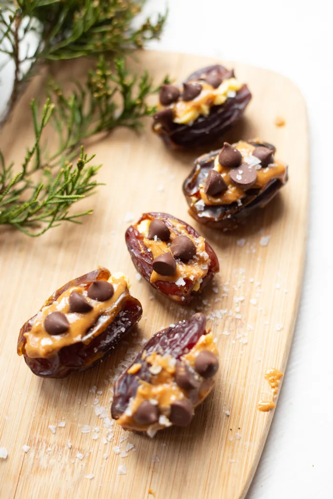 stuffed dates with peanut butter and chocolate chips sitting on a wooden cutting board, surrounded by salt sprinkles